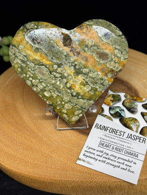 Rainforest Jasper heart crystal carving on clear acrylic stand with earthy green and brown patterns.