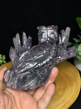 Load image into Gallery viewer, Hand holding a crystal purple mica lepidolite sculpture against a dark background
