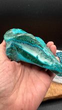Load image into Gallery viewer, A hand holding a polished natural stone with vibrant turquoise and deep green banded patterns, set against a dark background.
