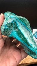 Load image into Gallery viewer, A hand holding a polished natural crystal specimen with vibrant turquoise and green banded patterns, set against a dark background.
